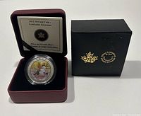 Coin in protective case inside burgundy presentation box, with black outer box and certificate visible.