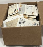 Open cardboard box filled with numerous first day covers and other postal covers piled inside, some with visible postage stamps and postmarks.
