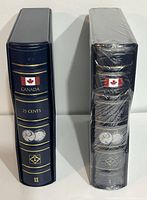 Pair of blue Canada 25 cents coin binders, one sealed and one open, showing spine with Canadian flag and coin images.