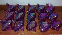 Photo showing 15 purple, ribbed, teardrop-shaped shatterproof Christmas ornaments, arranged in three rows on a wooden surface.
