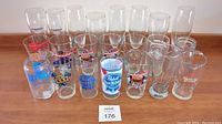 Top view of nineteen branded beer glasses arranged in rows on a wooden surface showing various beer logos including Widmer, Miller Lite, Pabst Blue Ribbon, Budweiser, Samuel Adams, and others.