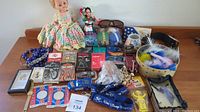 Wide view of assorted collectables including dolls, cards, toy cars, jewelry, and other memorabilia arranged on table
