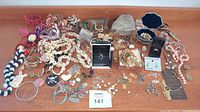 Overview photo of entire jewelry lot showing a broad variety of necklaces, bracelets, rings, earrings, and watches spread across a flat surface.