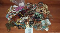 Photo showing a large pile of assorted costume jewelry on a wooden surface, including beaded necklaces, bracelets, and pendants.