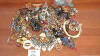 Overview of large assortment of jewelry laid on a wooden surface including many necklaces, bracelets, and earrings of varying materials and colors.