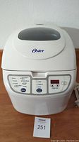 Front view of Oster bread maker showing digital control panel and brand logo.