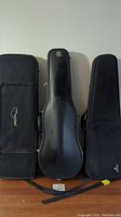 Three black violin cases side by side showing size and design