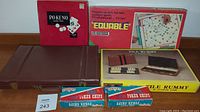 Front view of all boxed vintage games and poker chips including Pokeno, Equable, Tile Rummy, and three poker chip boxes on a table.