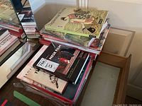Stack of hardcover Asian art and culture books on a wooden surface near a mirror.