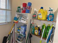 Shelf and unit containing cleaning towels, J-cloths, dish soaps, spray bottles, and detergent bottles.