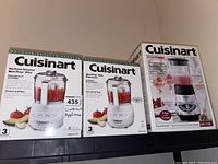 Photo showing two boxed Cuisinart Mini-Prep Plus Processors and one boxed Cuisinart SmartPower Chrome Blender stacked on shelf.