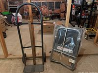 Vertical hand truck with wooden plank reinforcement beside packaged platform hand truck.