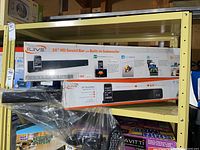 Two boxed sound bars on shelf with unboxed units and remotes below