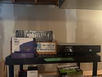 Overall view of two laptop AC adapters in boxes, shrink-wrapped rectangular speaker on top of a plastic shelving unit with Sony DVD player