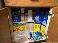Photo shows inside cabinet with multiple boxes of Glad garbage bags, Kitchen Catchers, Ziploc containers, and dishwasher detergent bottles.