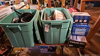 Two large green plastic bins filled with kitchen items such as frying pans, utensils, and boxes