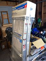 Upright view of ladder in original wrapped packaging among other stored items