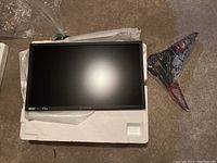 Monitor resting in styrofoam packaging with protective wrap, stand base beside it