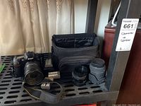 Shelf overview with Nikon D80 and attached 18-200mm lens, two extra lenses, strap, two batteries, charger, and camera bag