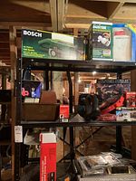 Bosch belt sander in box, electric duster, and other boxed tools on metal shelving.
