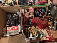 Image showing boxed Schlage locks, screwdriver sets, assorted hardware in cardboard box and white caddy, with a red metal toolbox on the right and some metallic spray canisters below.