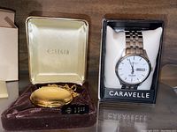 Both watches displayed with their original boxes: Elgin pocket watch in brown velvet box and Caravelle wristwatch in black presentation box with label