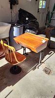 Side view of antique wooden school desk and matching wooden chair with iron bases, placed indoors on concrete floor.