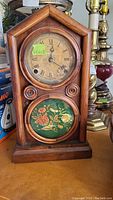 Front view of antique mantle clock with shaped wooden frame and glass floral lower panel.
