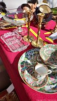All items displayed on red tablecloth including Asian style plate and bowls, brass candlesticks, clear crystal bowl, and glass divided dish.