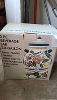 Box with printed image and description of the 3.8 gallon beverage jar and base bowl, showing the hand-painted ceramic design.