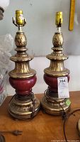 Pair of brass-toned and red ceramic lamps on wooden surface without lampshades or harps. Each lamp approximately 22 inches tall.