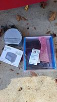 Photo showing iHome clock radio, Garmin device in protective packaging, and iHome instruction manual on pavement with dry leaves.