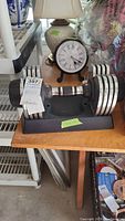 Adjustable dumbbell set shown on black plastic stand alongside clock and other items, displaying overall condition and stand.