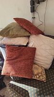 6 assorted throw pillows stacked showing various fall tones and textures needing cleaning with pet hair visible