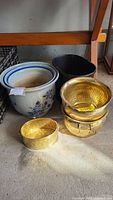 Overview of six items: two blue floral ceramic planters, two gold-toned metal planters, one oval black metal waste can, and one large oval black metal planter arranged on the floor.