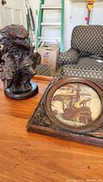 Resin wolf and eagle sculpture next to the framed Artini ship engraving on a wooden surface with background furniture