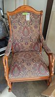 Full view of the carved wood rocking chair showing brocade fabric upholstery on seat and back