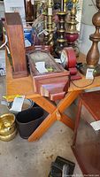 Wood trestle table surface with a wooden pendulum clock and various metal candlesticks on top, showing scratches on the surface and the crossed leg base.