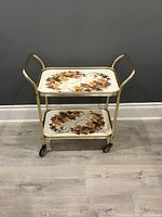 Full front view of the vintage mid century cocktail bar cart with two trays decorated in floral pattern.