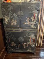 Full view of the black lacquered two-piece Chinese cabinet showing hand-painted scenes and metal hardware.