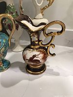 Dark vase with gold accents and deer motif beside a brightly colored floral vase on a white surface.