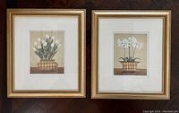 Two framed floral prints side by side, one with tulips and one with orchids, both in gold-toned harlequin-patterned vases.