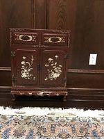 Front view of lacquer cabinet with mother-of-pearl inlay against wood panel wall on decorative rug