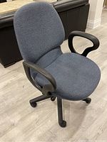 Side angle photo showing blue fabric seat and backrest, black curved armrests, and black base with casters.