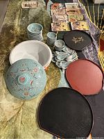 Top view showing big lidded bowl, small bowls, spoons, rectangular plates, and fan-shaped trays arranged together on fabric.