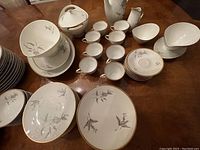 Various plates, bowls, cups and serving pieces arranged on a wood table showing the floral and gold trim design