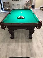 Full view of table from one end showing wood frame, green felt and pocket fringe