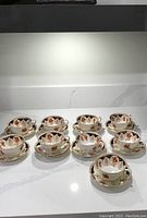 Eight delicate teacups and saucers arranged on a counter showing the full set.