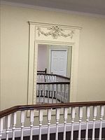 Full view of the large cream painted wood trumeau mirror reflecting staircase and door in background.