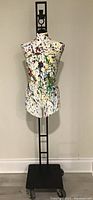 Front view of the dress form mannequin showing the splattered paint design on the torso and the black iron stand.